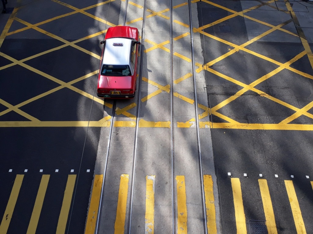 A red taxi drives past a crosswalk through a deserted downtown street.
