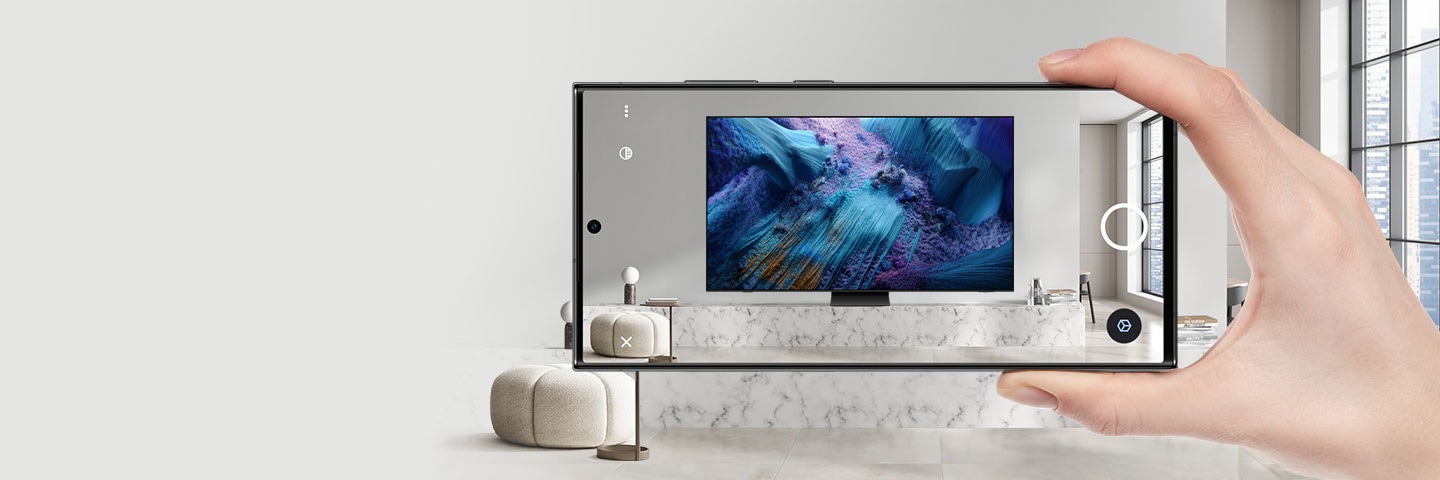 A person is holding a smartphone displaying Samsung's 98 inch Supersize TV on its screen, demonstrating the availability for exploration through AR.