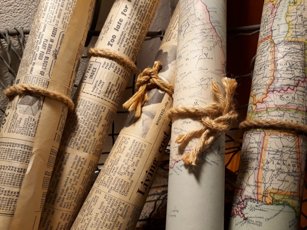 A set of rolled up maps and newspapers clippings fastened with binder twine in a basket.