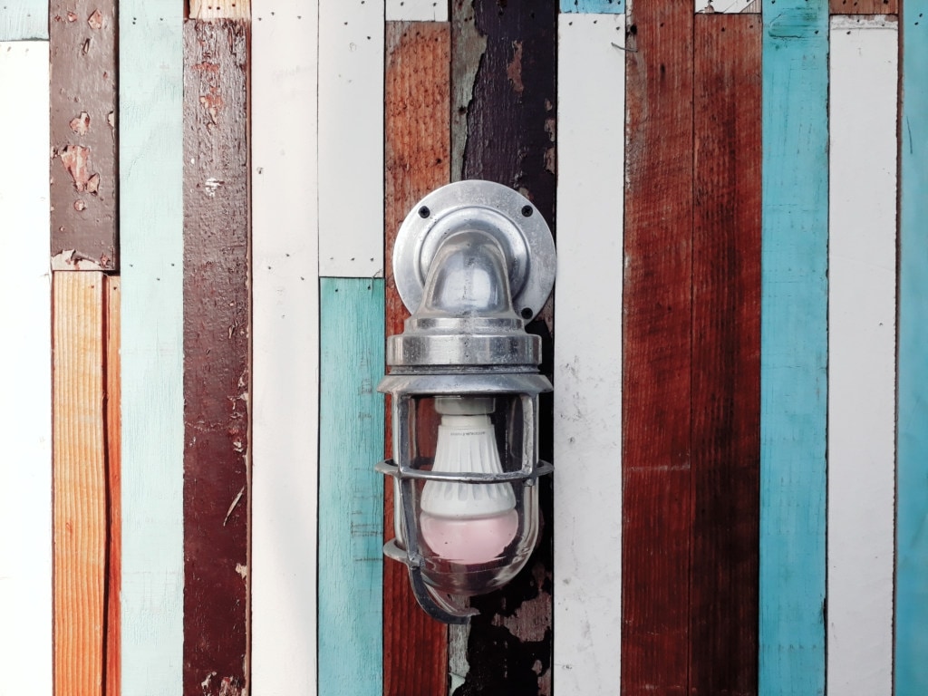 A lone porch light hangs against a weathered wooden wallfront.