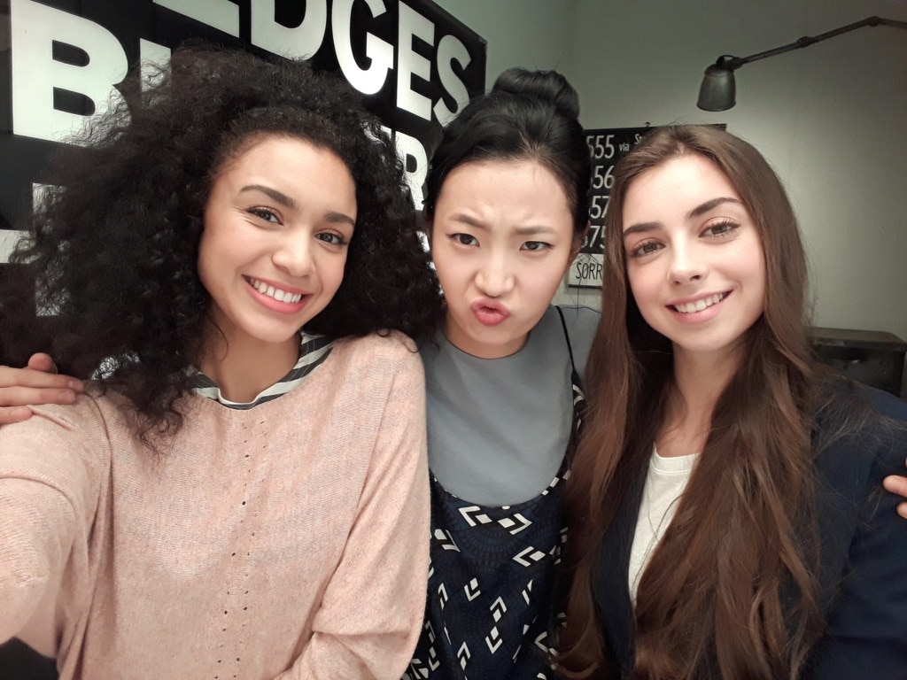 Group selfie shot of three models posing on set.