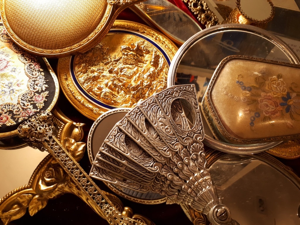 An assortment of ornate antique mirrors and fans spread out over a vanity.